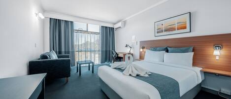 Habitación de hotel con una cama grande, un escritorio, una silla, un sofá y vistas al exterior.