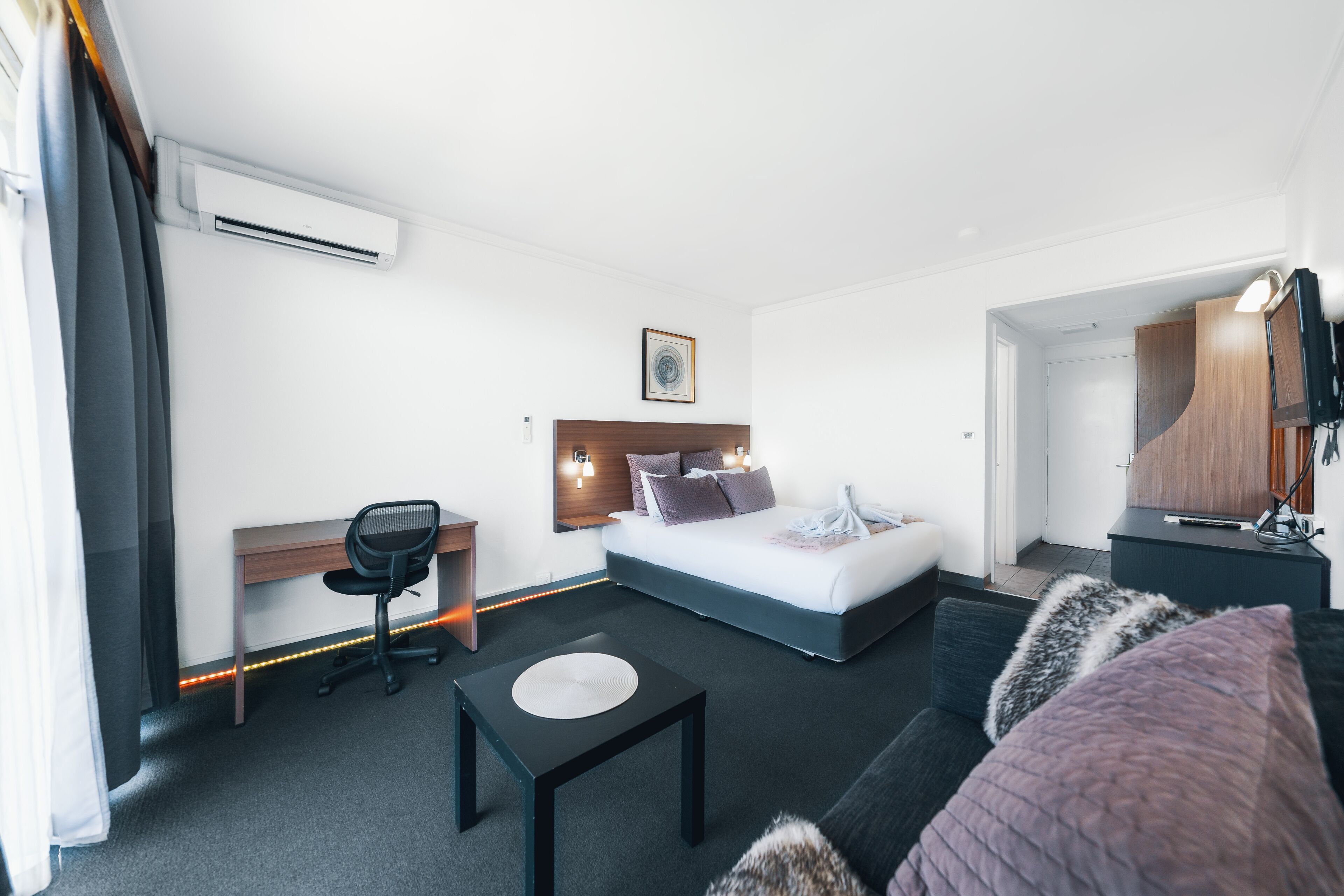 A modern hotel room with a bed, desk, chair, and a small table.