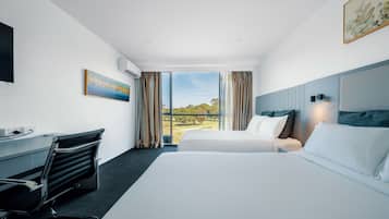 A modern hotel room with a large bed, a desk, and a view of a park.