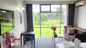 Une chambre d’hôtel équipée d’un bureau, d’un canapé, d’une télévision et d’une grande fenêtre donnant sur un terrain de golf.