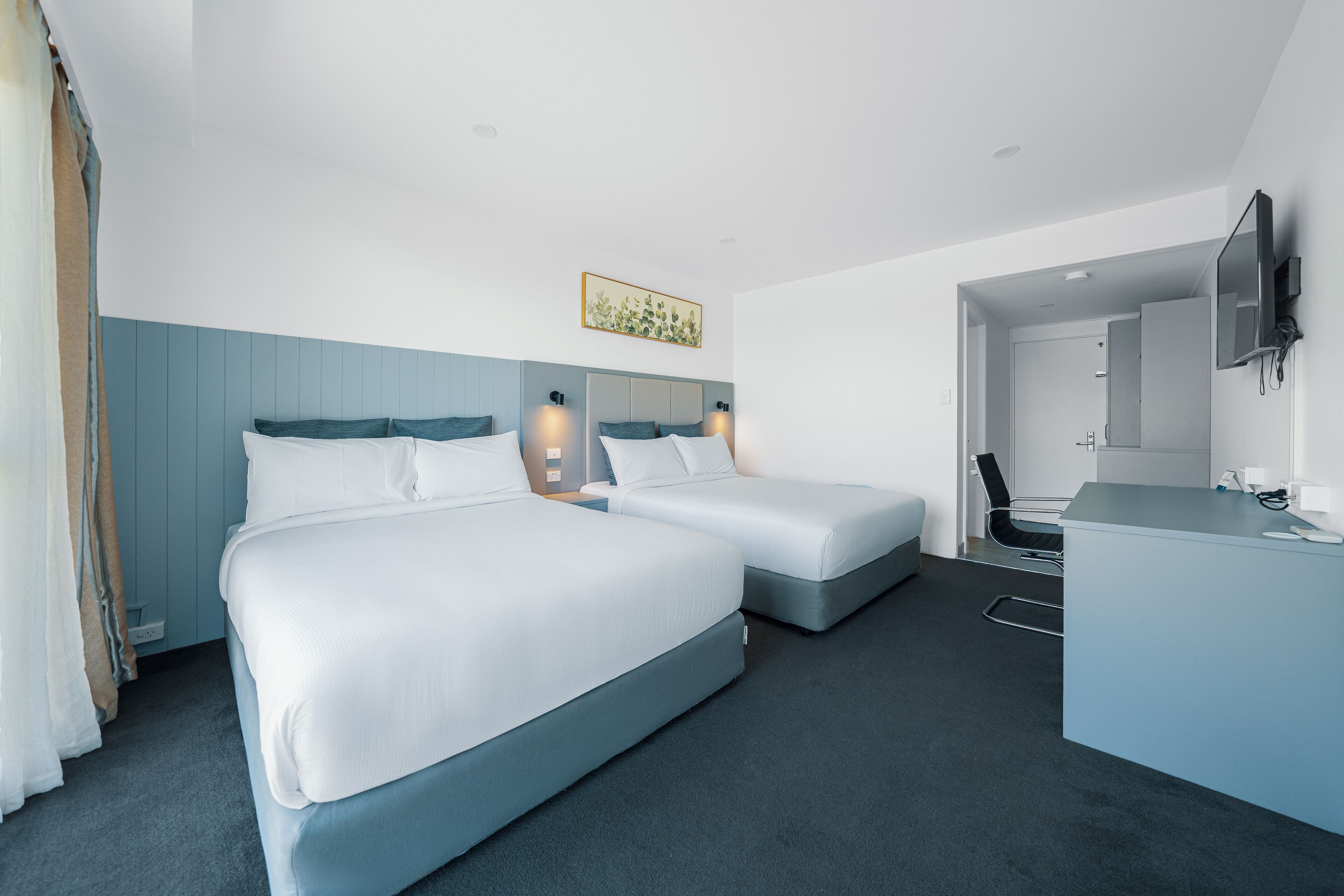 A hotel room with two beds, a desk, a chair, and a TV.