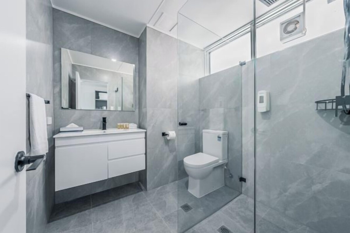A modern bathroom with a glass shower enclosure, a white toilet, and a vanity with a mirror.