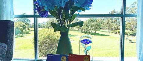 A window with a view of a golf course, a vase with blue flowers, and two books titled "Peppero Peppero".