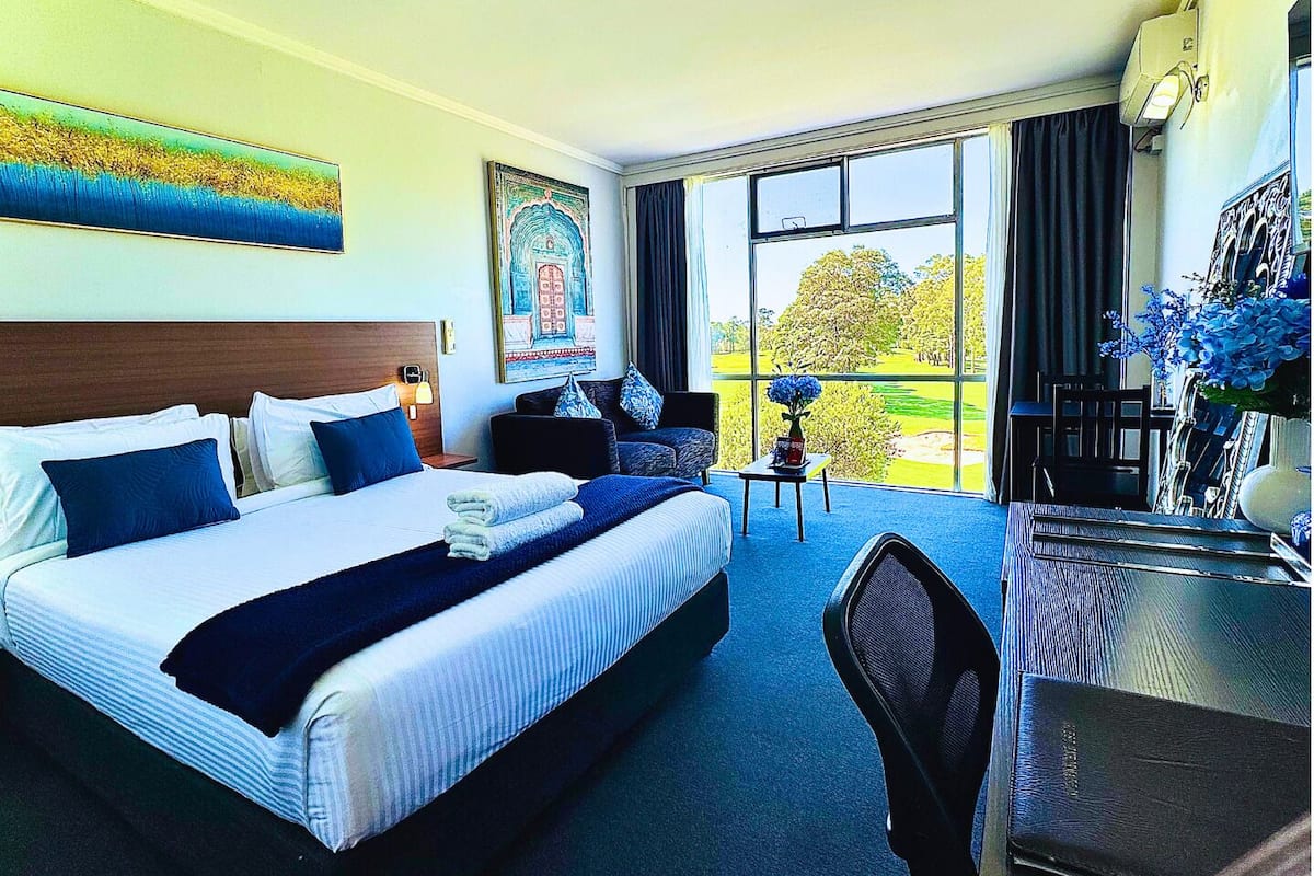 A hotel room with a large bed, a desk, and a view of a golf course.
