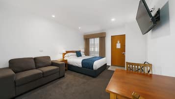 Une chambre d’hôtel avec un lit, un canapé, une table en bois et un téléviseur fixé au mur.
