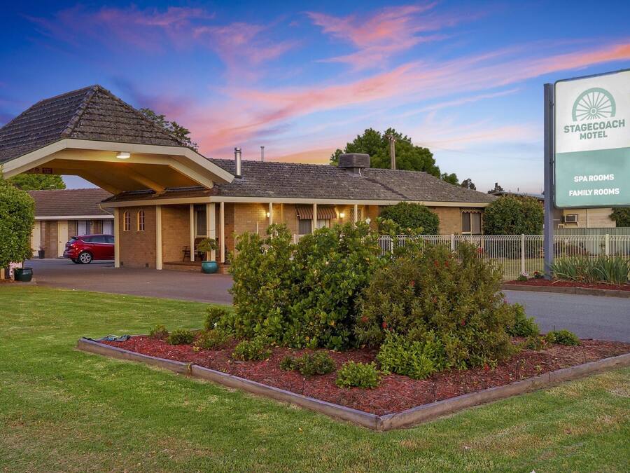 Un motel doté d’une entrée abritée, d’un jardin aménagé et d’une enseigne indiquant la présence d’un espace bien-être et de chambres familiales.