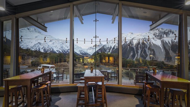 Un restaurante con vistas a la montaña, que cuenta con mesas y sillas de madera, y ventanas amplias.