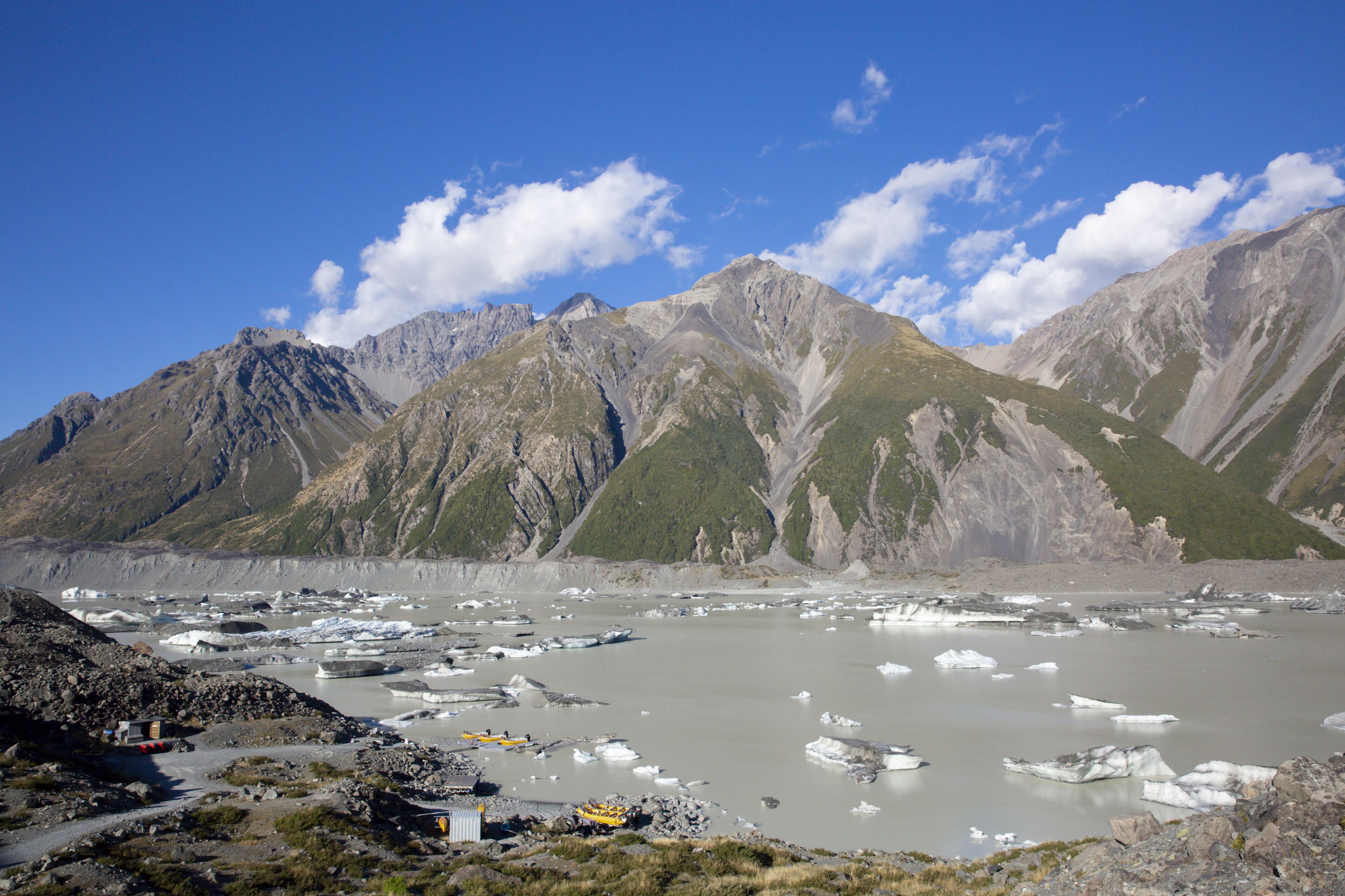 A mountainous landscape with a glacier and icebergs, a small building, and a clear sky.