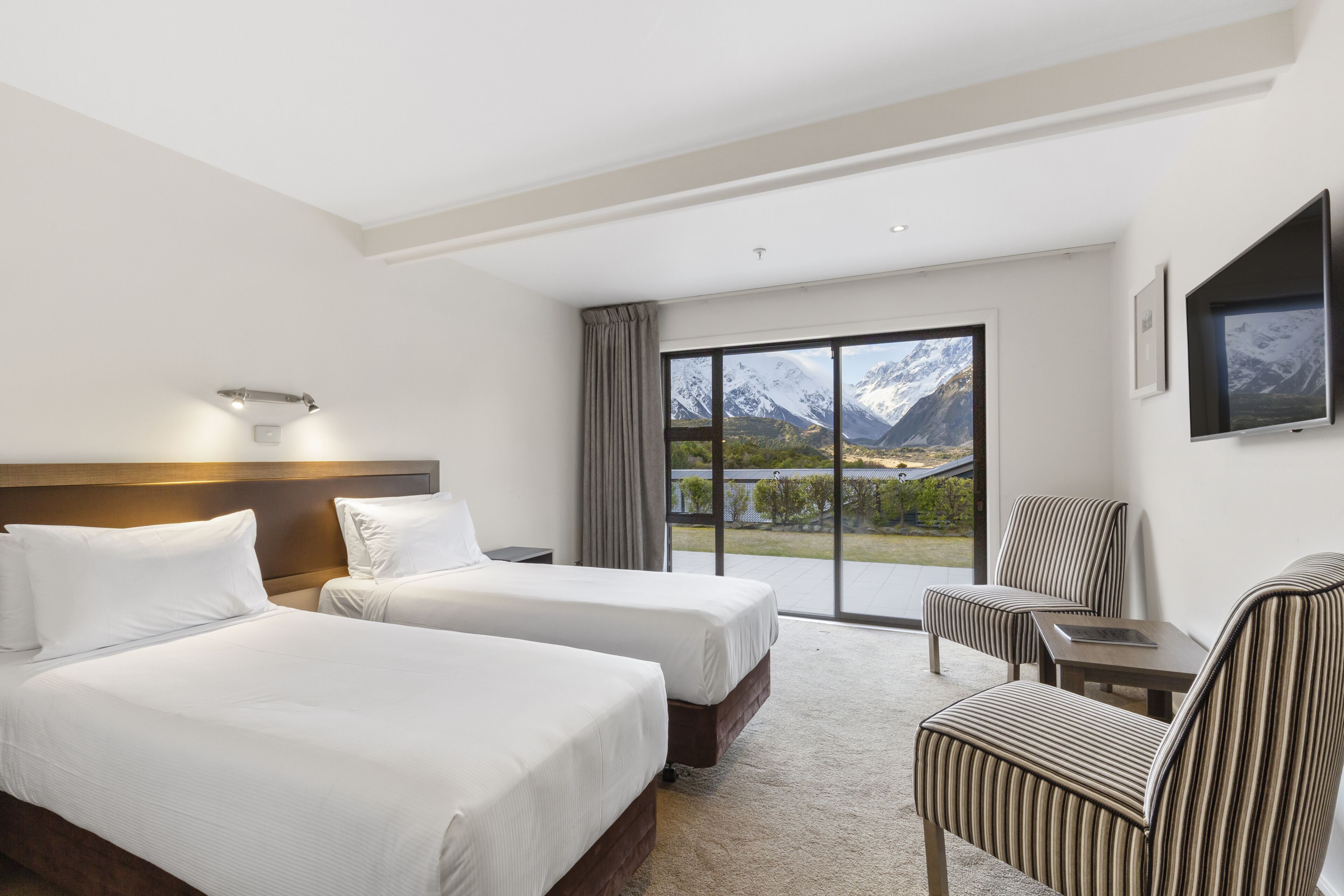 Ett hotellrum med två sängar, en TV, en stol och ett stort fönster med utsikt över bergen.