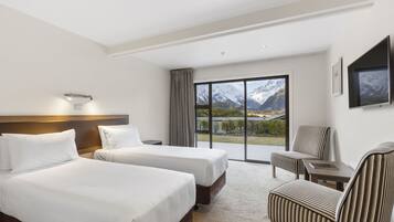 Ett hotellrum med två sängar, en TV, en stol och ett stort fönster med utsikt över bergen.