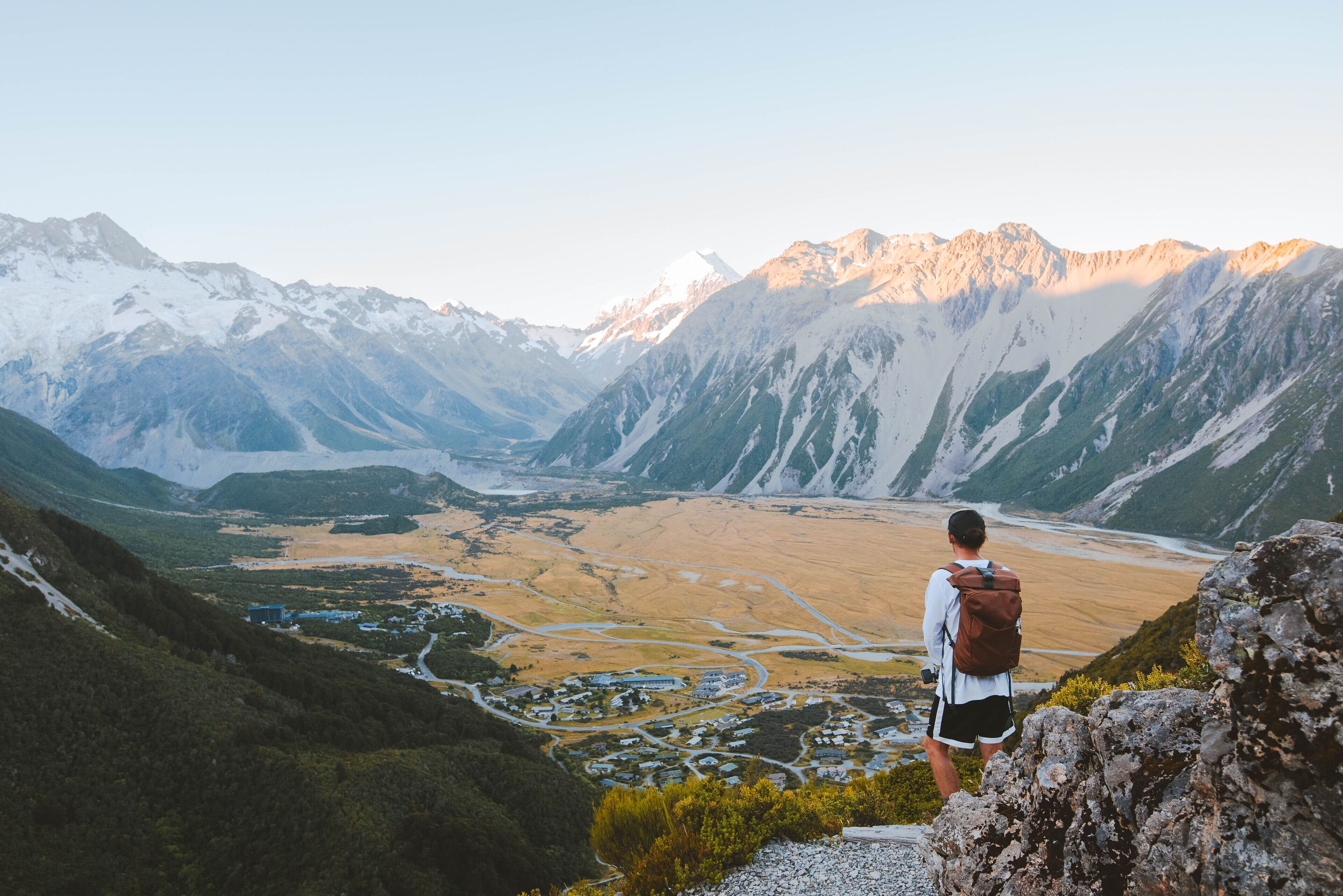 A hiker with a backpack overlooking a valley with mountains in the background.