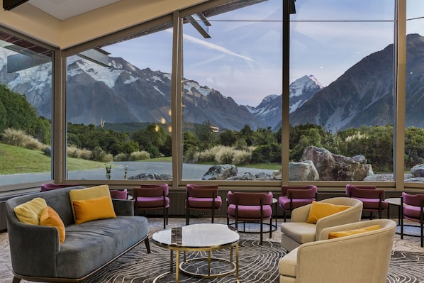 A modern interior with a sofa and chairs facing large windows with a mountain view. - The Hermitage Hotel Mount Cook (Mount Cook)
