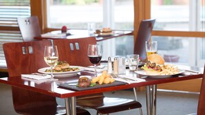 Un ambiente de restaurante con sillas de madera, una mesa con platos de comida, copas de vino y una hamburguesa.