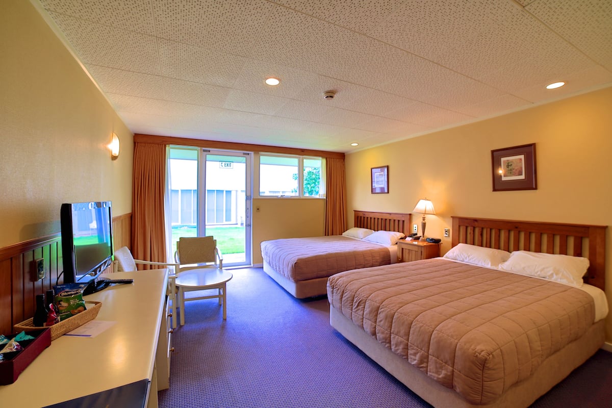 Une chambre d’hôtel avec deux lits, un bureau avec une télévision, une chaise et une fenêtre avec des rideaux.