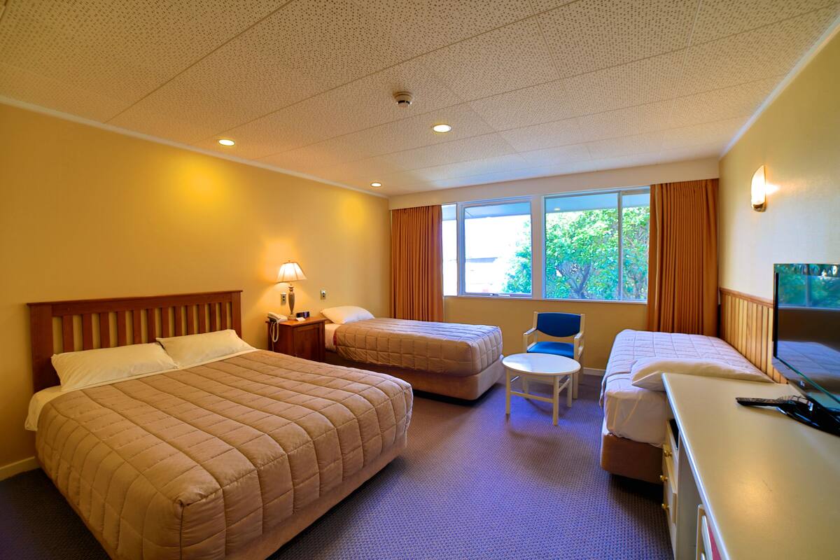 Une chambre d’hôtel avec deux lits, un bureau, une chaise et une fenêtre avec des rideaux.