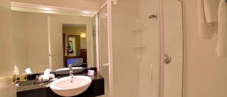 Un baño con lavamanos blanco, espejo y ducha con mampara de vidrio.