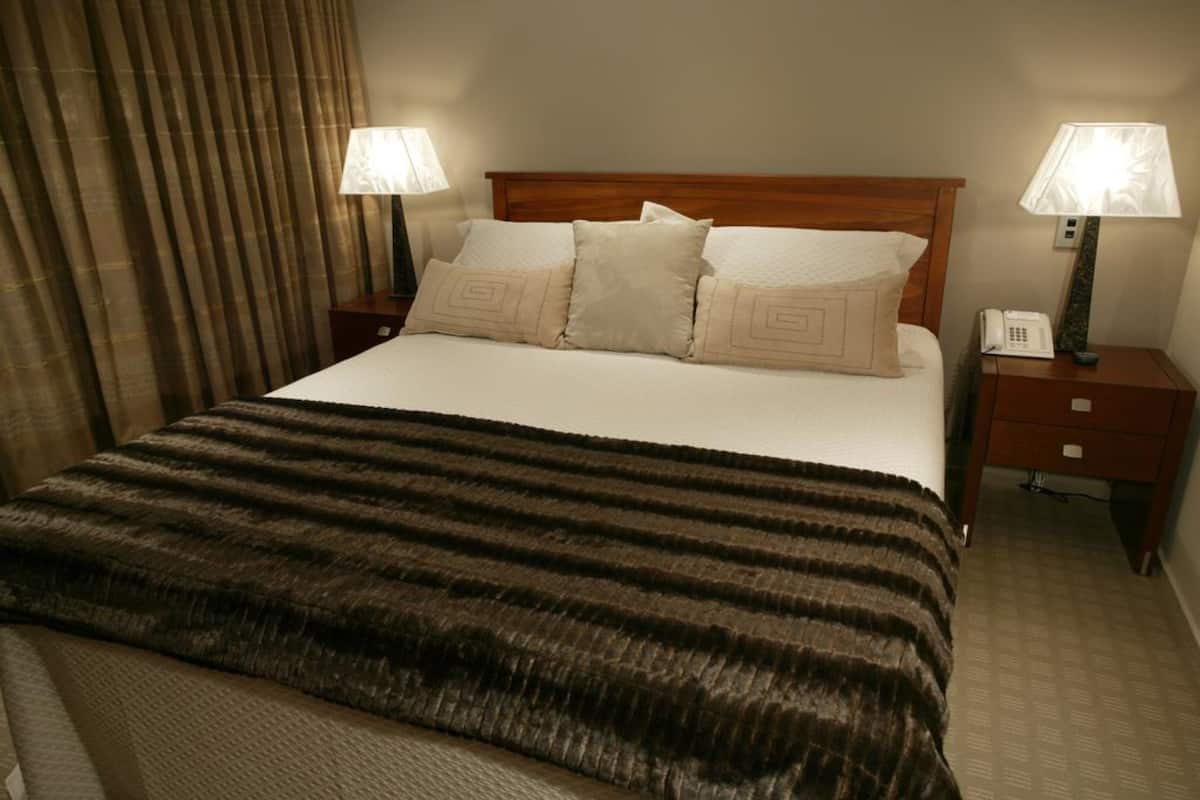 Une chambre d’hôtel avec un grand lit, deux tables de chevet avec des lampes, une tête de lit en bois et une couverture à rayures.