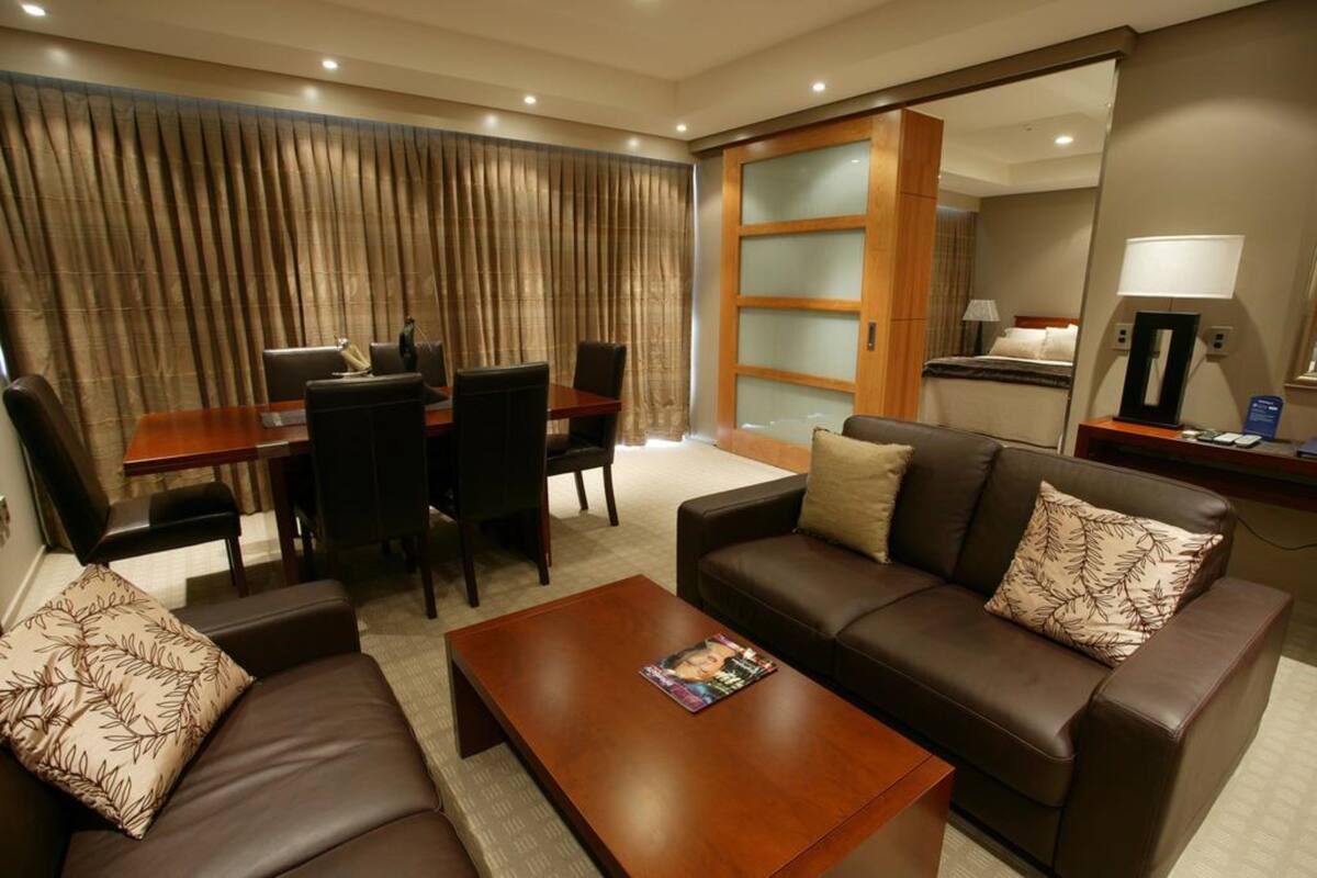 Une chambre d’hôtel moderne comprenant un coin salon, une table à manger avec des chaises, un canapé, une table basse et un grand miroir.