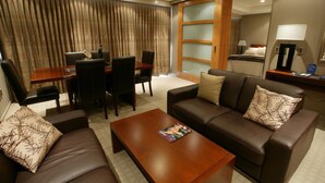Una habitación de hotel moderna con zona de estar, una mesa de comedor con sillas, un sofá, una mesa de centro y un espejo grande.