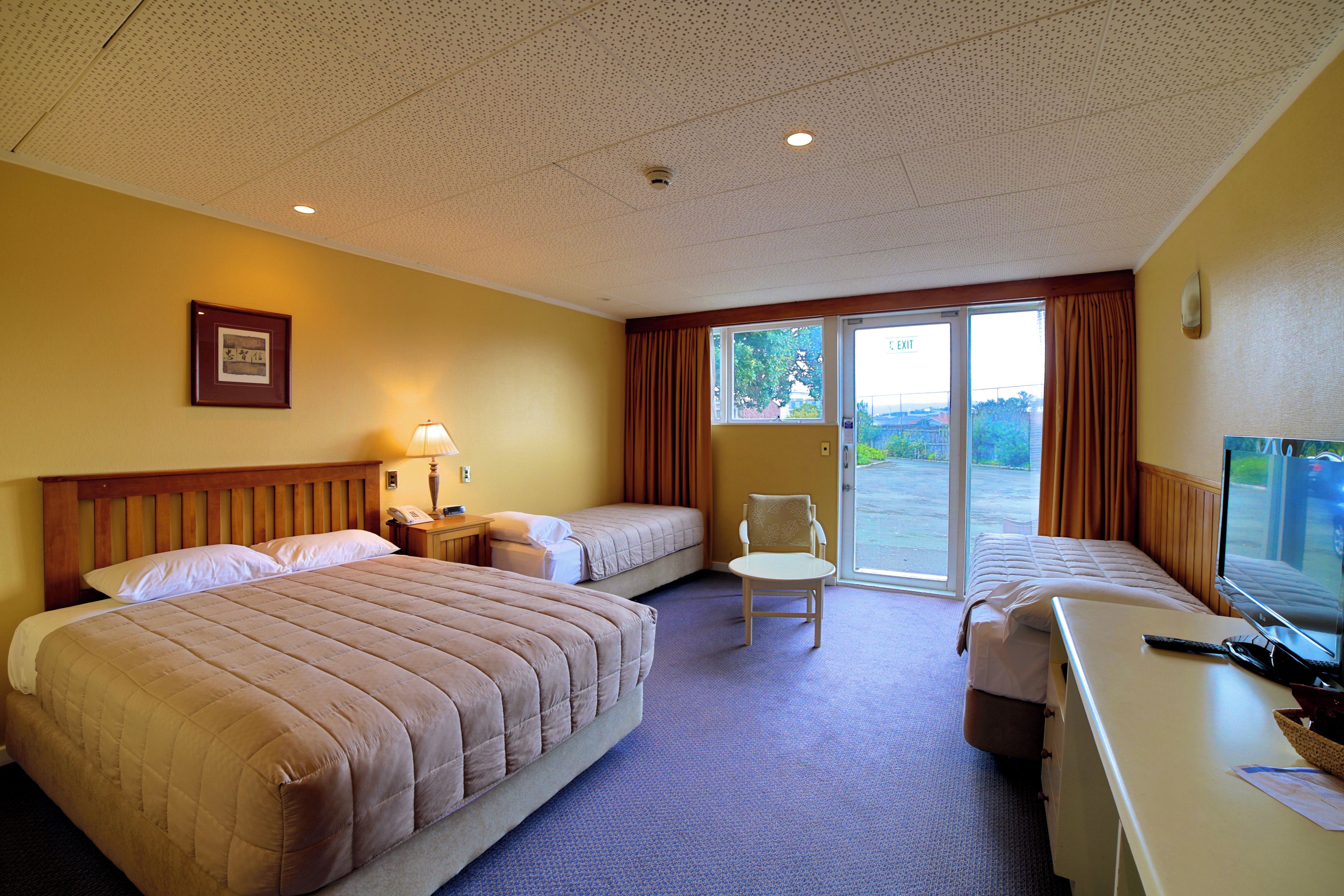 A hotel room with two beds, a desk with a TV, a chair, and a window with curtains.