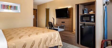 A hotel room with a bed, a desk with a computer, a television, a microwave, and a refrigerator.