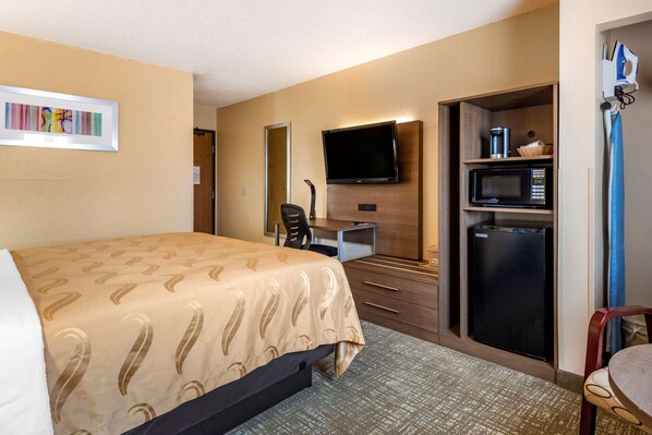 Una habitación de hotel con cama, escritorio con computadora, televisión, microondas y refrigerador.