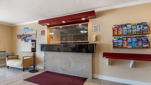 Un área de recepción con mostrador de mármol, un banco rojo, una silla, un teléfono instalado en la pared y un estante con libros de viajes.