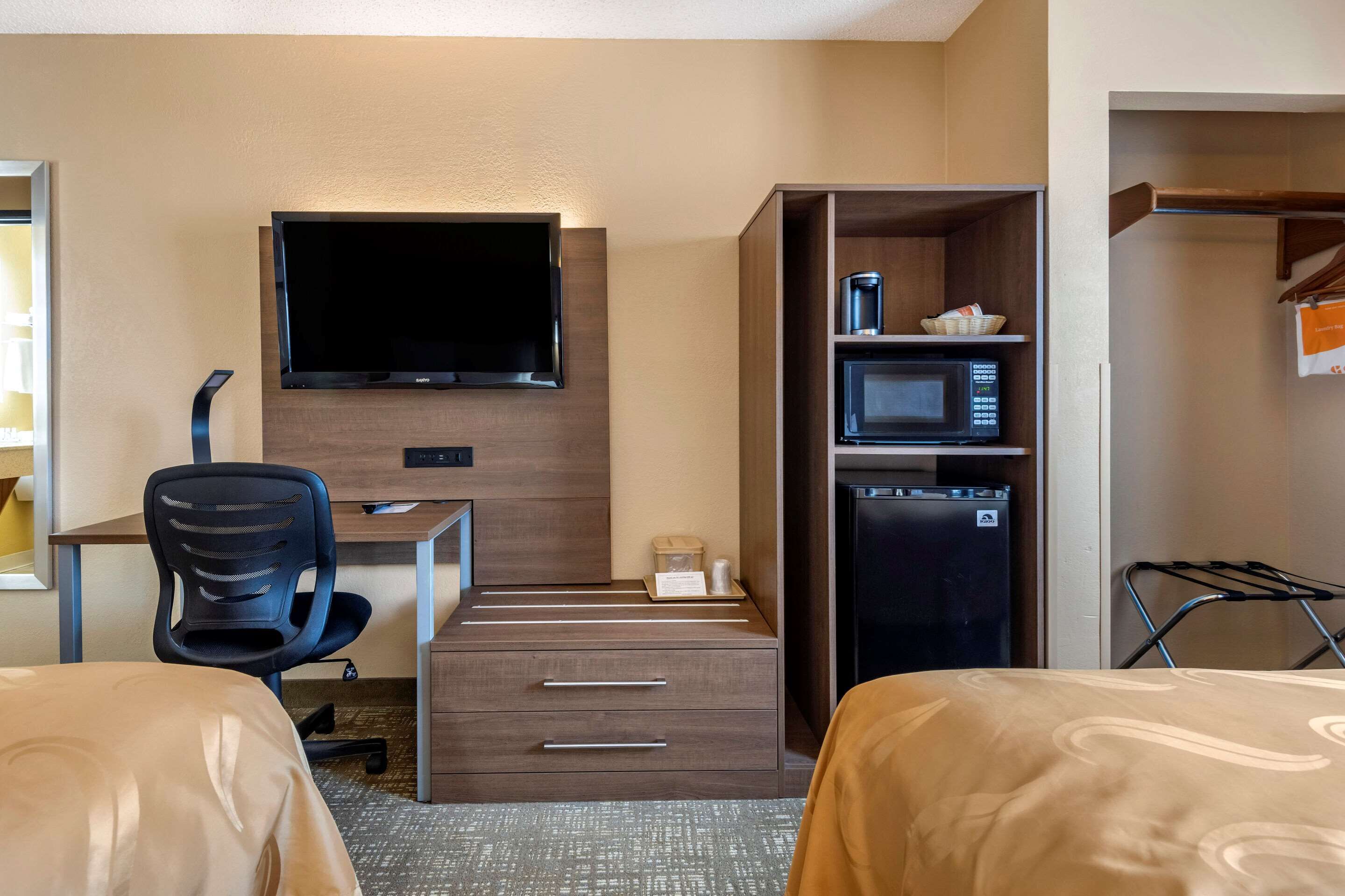 Een hotelkamer met een bed, een bureau met stoel, een televisie, een magnetron en een koelkast.