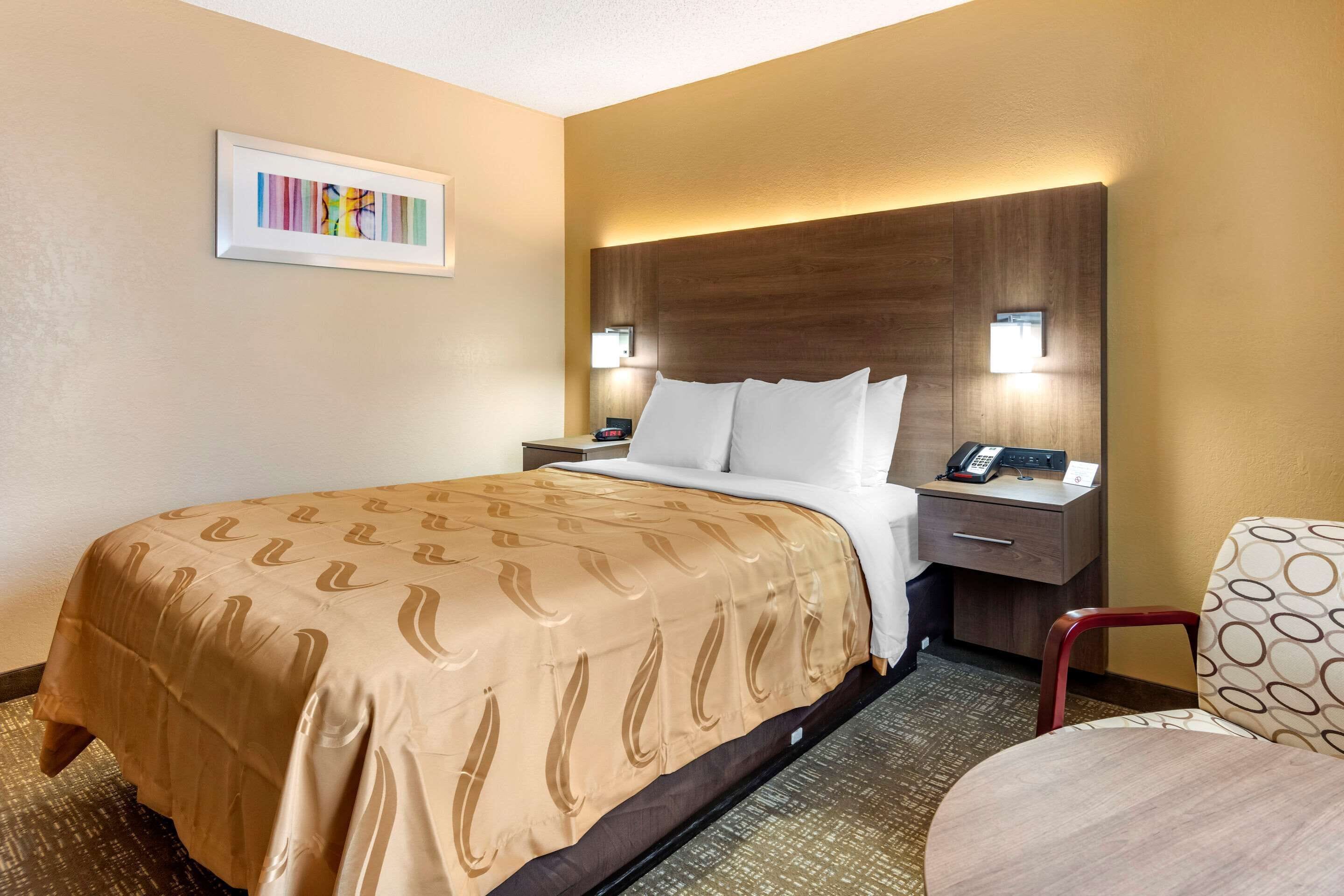 Una camera d'albergo con un letto, un comodino, una sedia e un quadro appeso al muro.