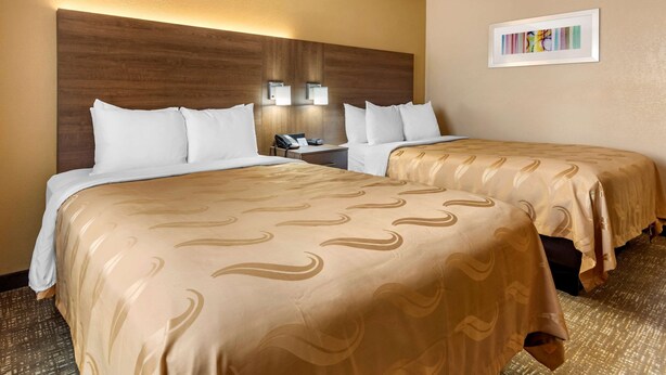 Habitación de hotel con dos camas, cabecero de madera, lámparas de noche y una obra de arte enmarcada en la pared.