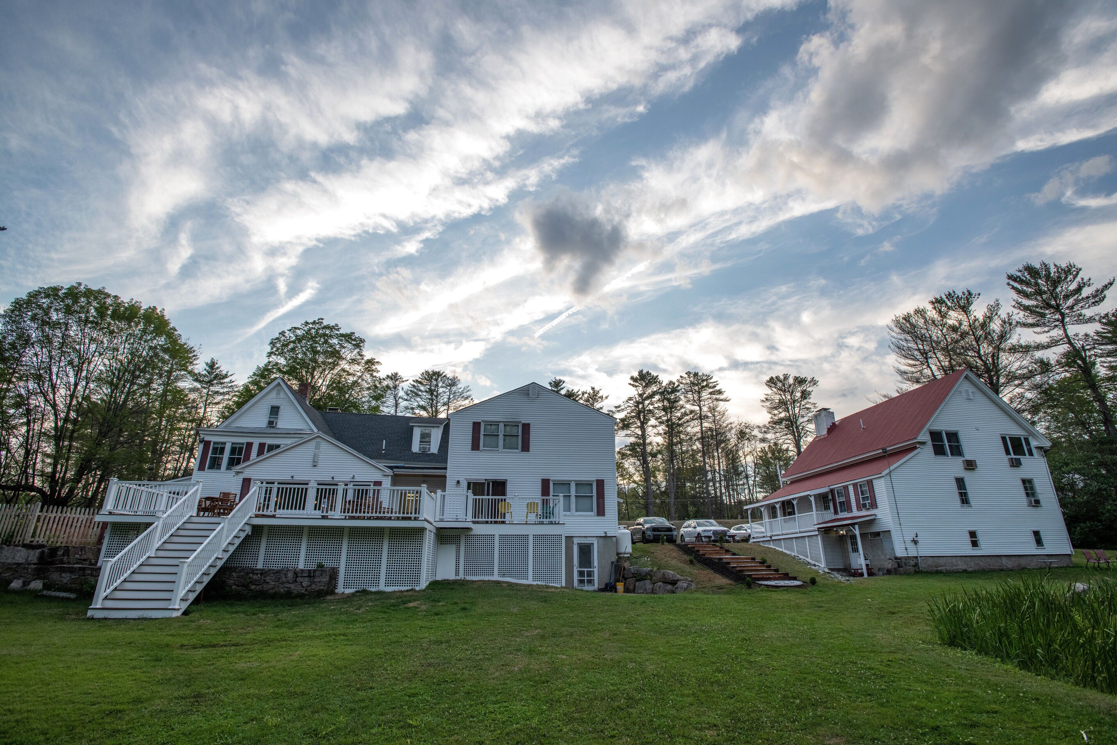 A large white house with a red roof, a front porch, and a staircase leading to a deck.