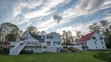 A large white house with a red roof, a front porch, and a staircase leading to a deck.
