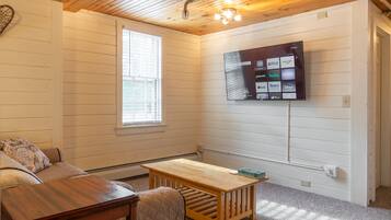 A cozy room with a wooden ceiling, a TV mounted on the wall displaying various streaming services, a small wooden table, and a cushioned bench.