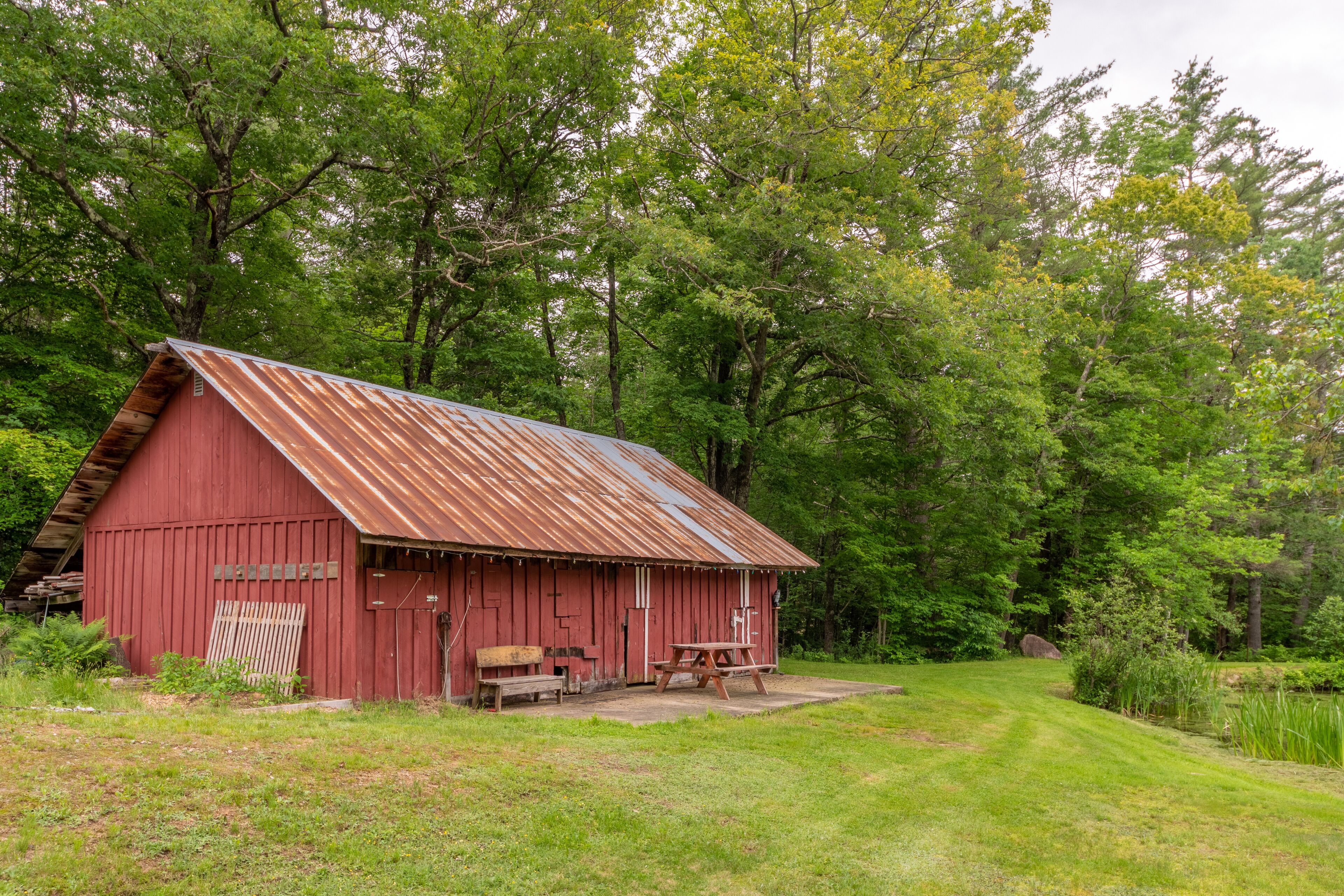 A red barn with a sloped roof, a picnic table, and benches in front.
