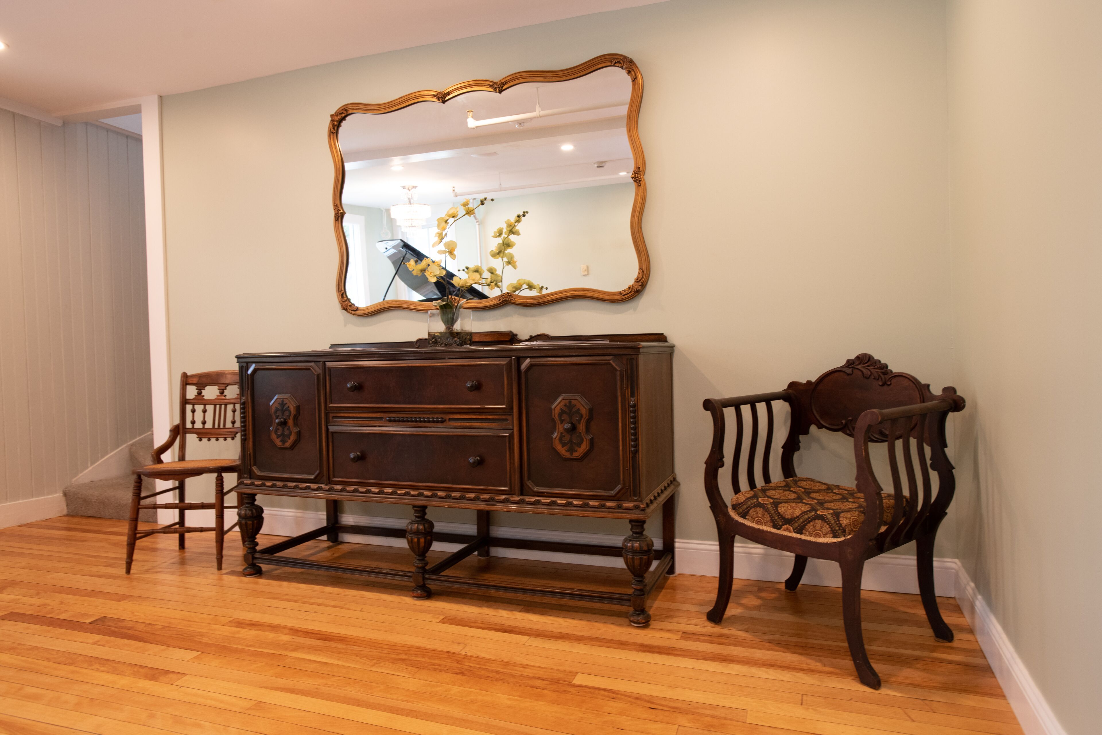 A room with a wooden dresser, a chair, and a mirror on the wall.