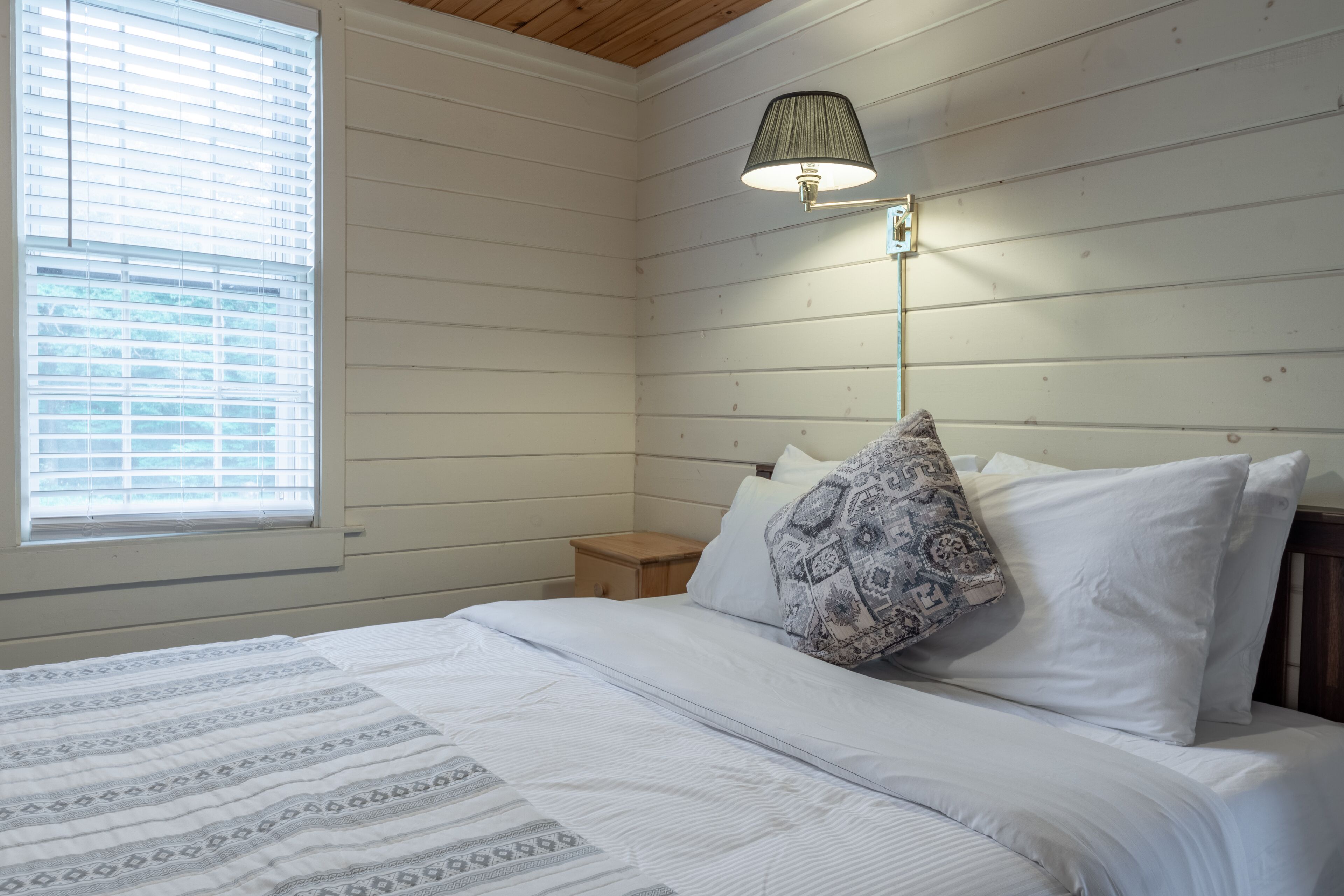 Een slaapkamer met een bed, nachtkastje, lamp en een raam met zonwering.