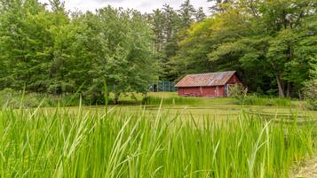 A rustic red barn surrounded by lush green trees and tall grass.