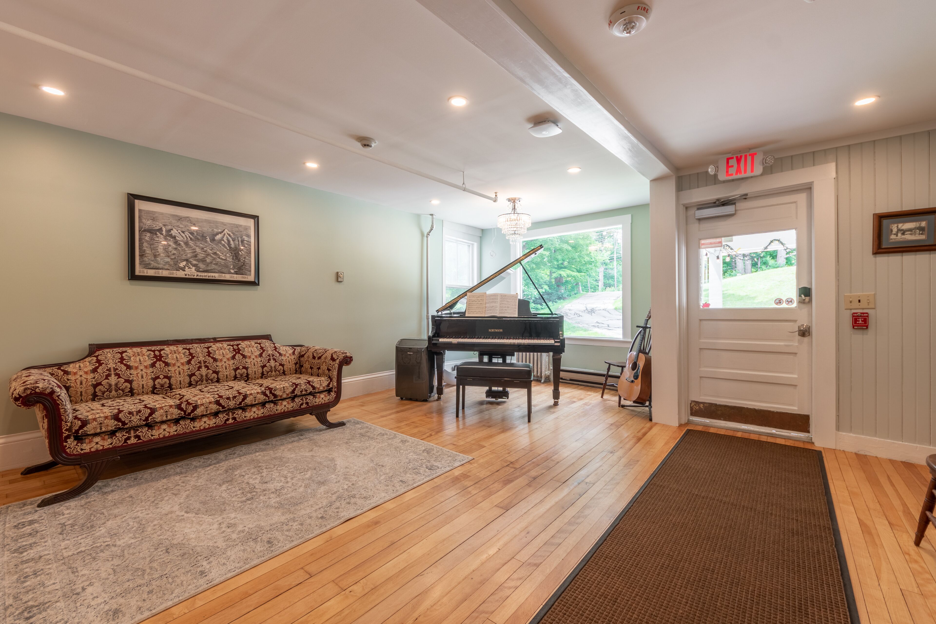 Una habitación amplia con un piano de cola, un sofá antiguo y un cuadro en la pared.