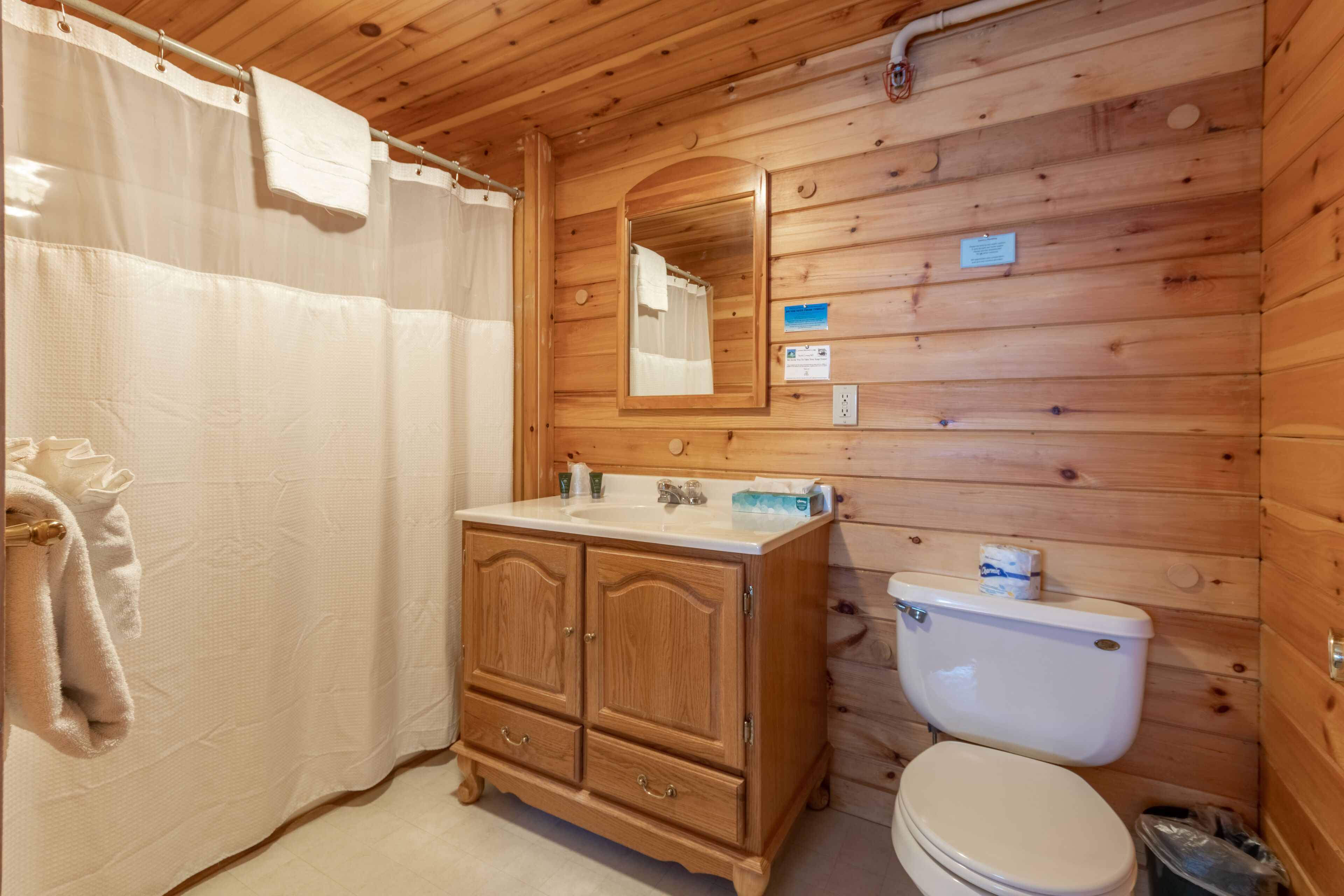 Een houten badkamer met een houten wastafel, toilet en douchegordijn.