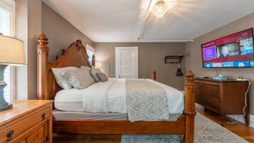 Un dormitorio con cama de dos columnas, cómoda de madera, televisor montado en la pared y candelabro.