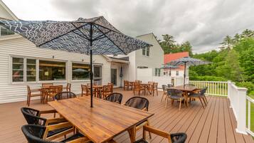 A wooden deck with outdoor furniture, including tables and chairs, and two umbrellas providing shade.