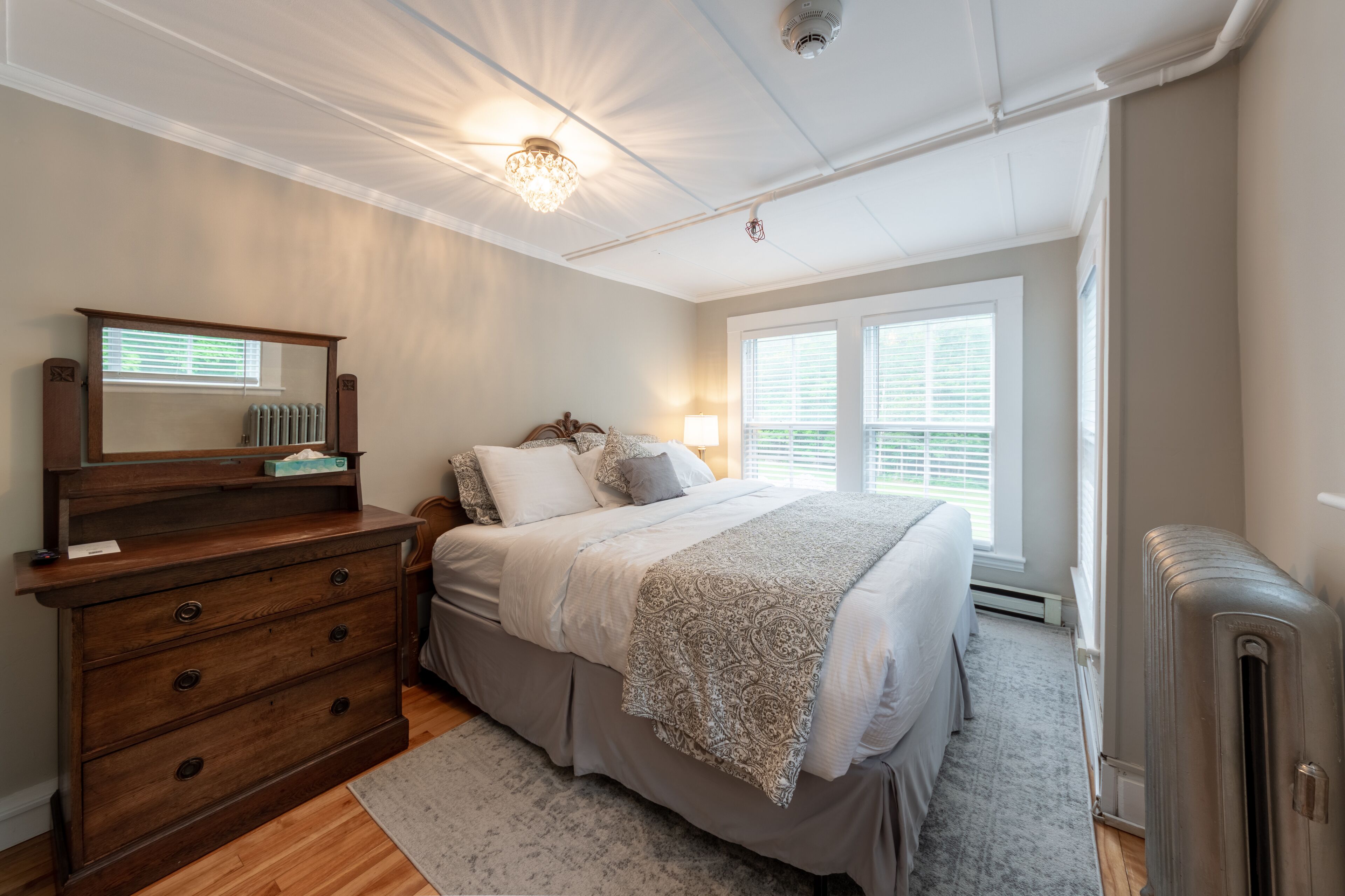 Un dormitorio con cama, cómoda, espejo y radiador.