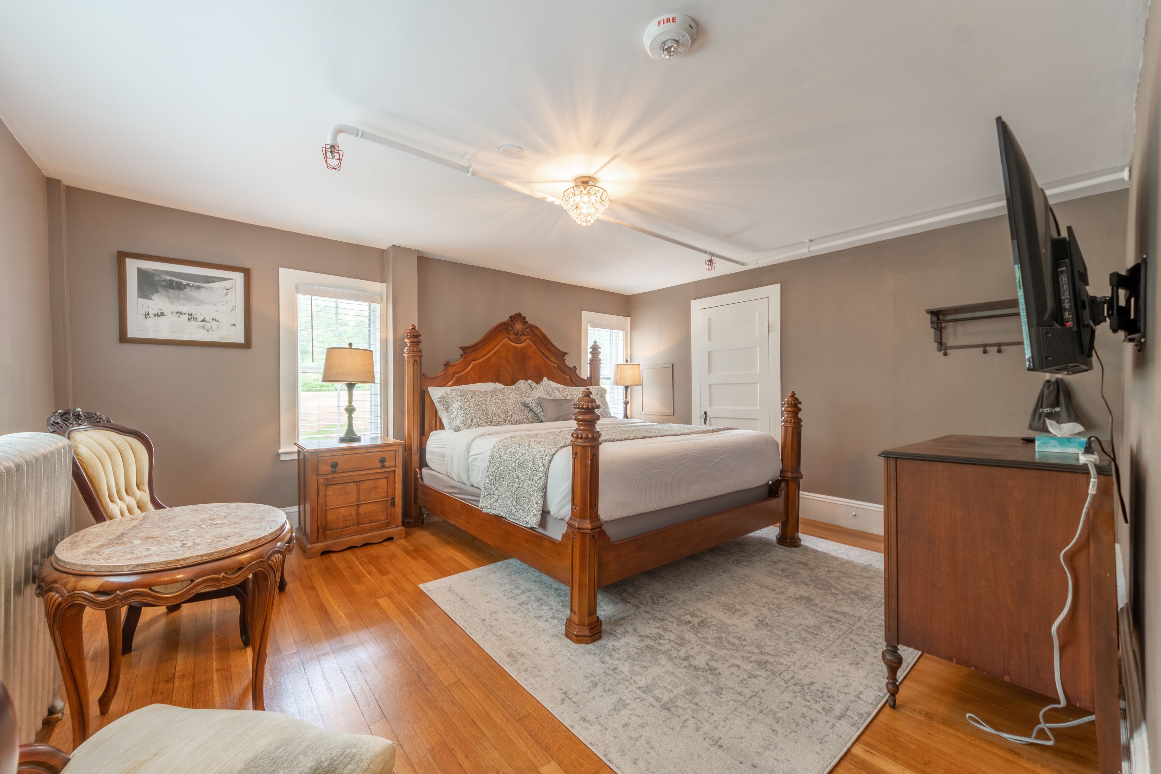 A bedroom with a wooden bed, a nightstand, a chair, a desk, and a television.