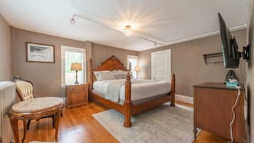 A bedroom with a wooden bed, a nightstand, a chair, a desk, and a television.