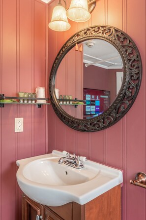 A bathroom with a white sink, a mirror with an ornate frame, and a shelf with toiletries. - Cranmore Mountain Lodge Bed & Breakfast (North Conway)