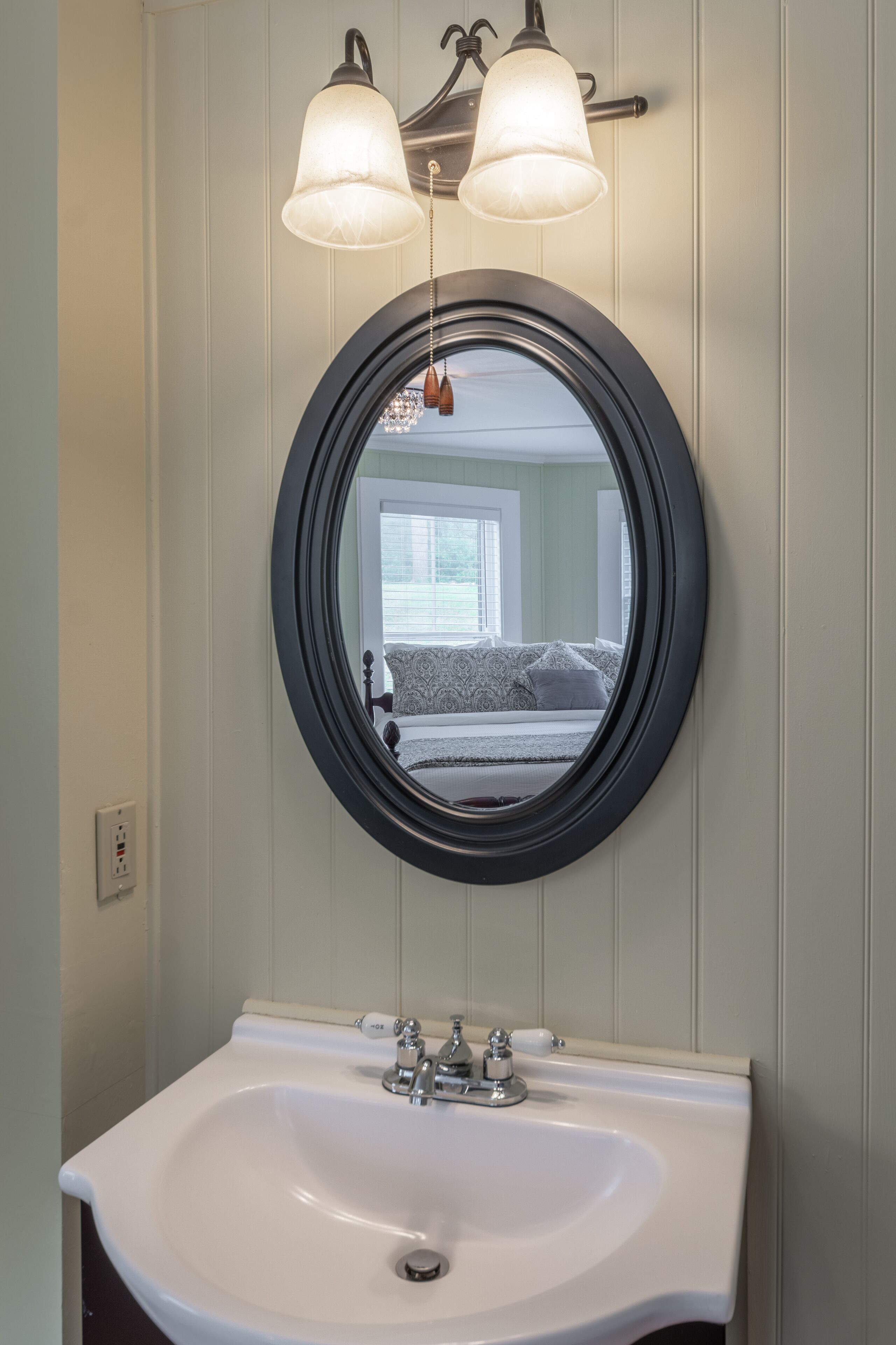 Un baño con un espejo redondo, un lavabo blanco y dos luces fijadas a la pared.