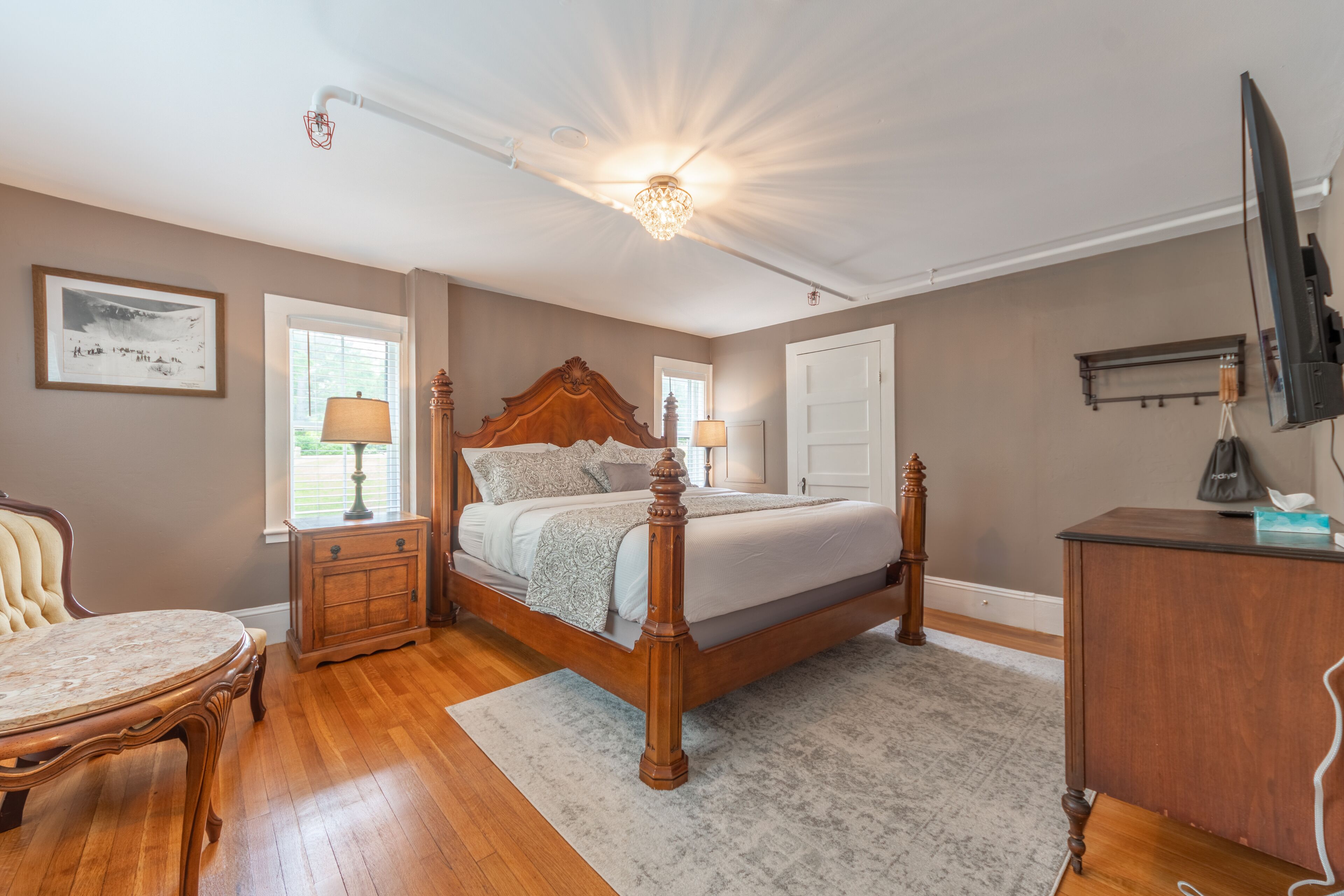 A bedroom with a wooden bed, a chair, a desk, and a television.