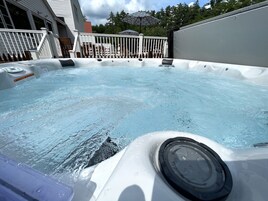 A hot tub with a white exterior and a metal cover, surrounded by a white deck and a white railing.