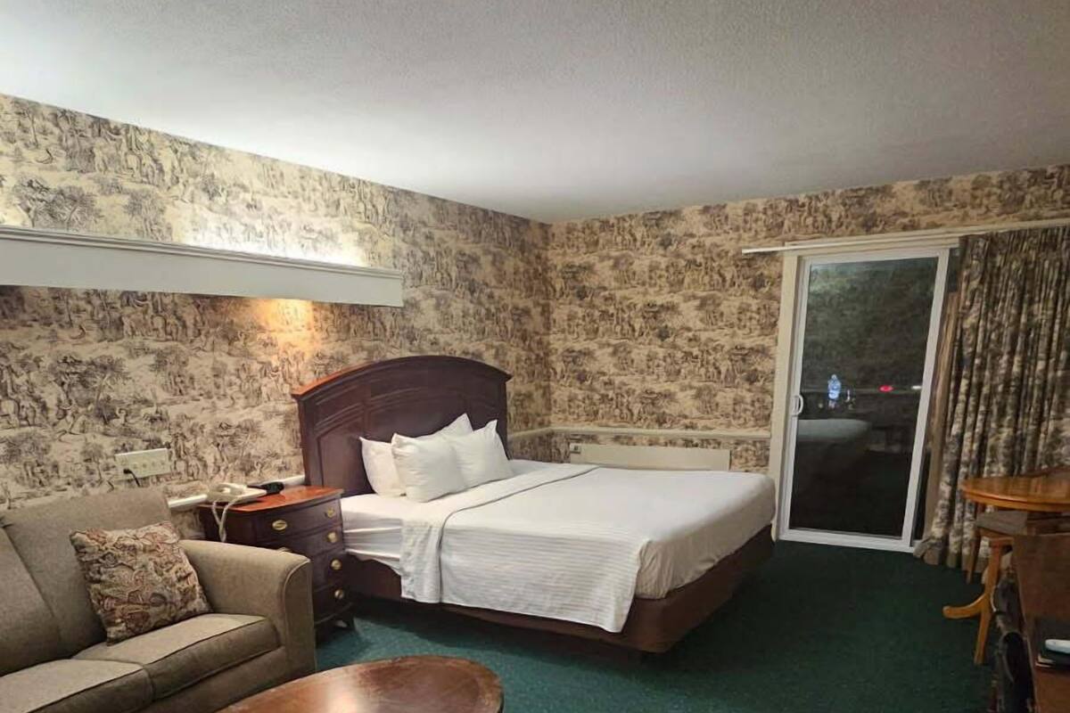 A hotel room with a bed, a sofa, a small table, and a carpeted floor.