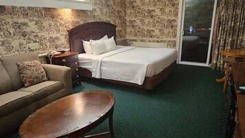 A hotel room with a bed, a sofa, a small table, and a carpeted floor.